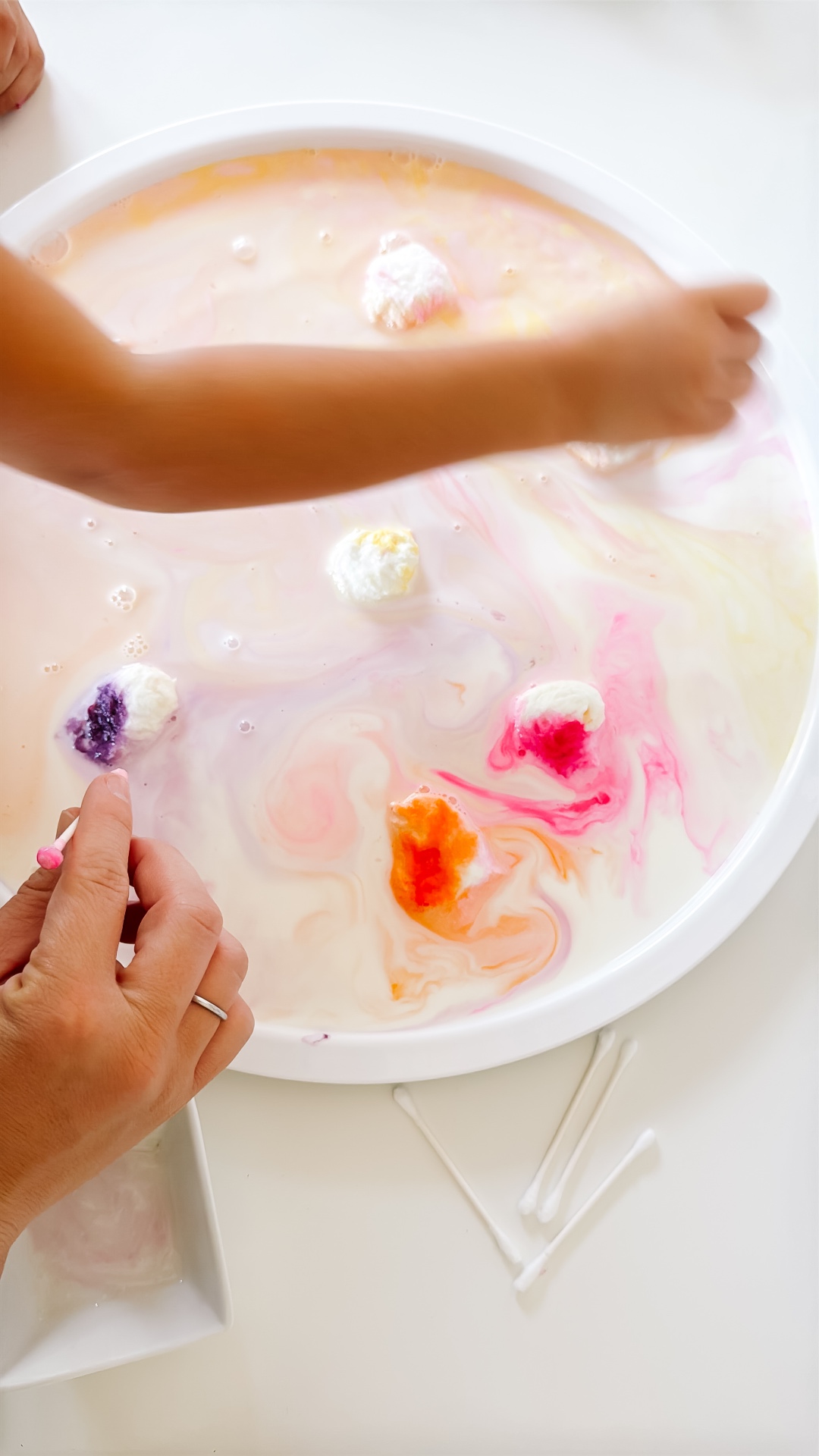 Adult and child touching soapy cotton swabs to colored spots in milk