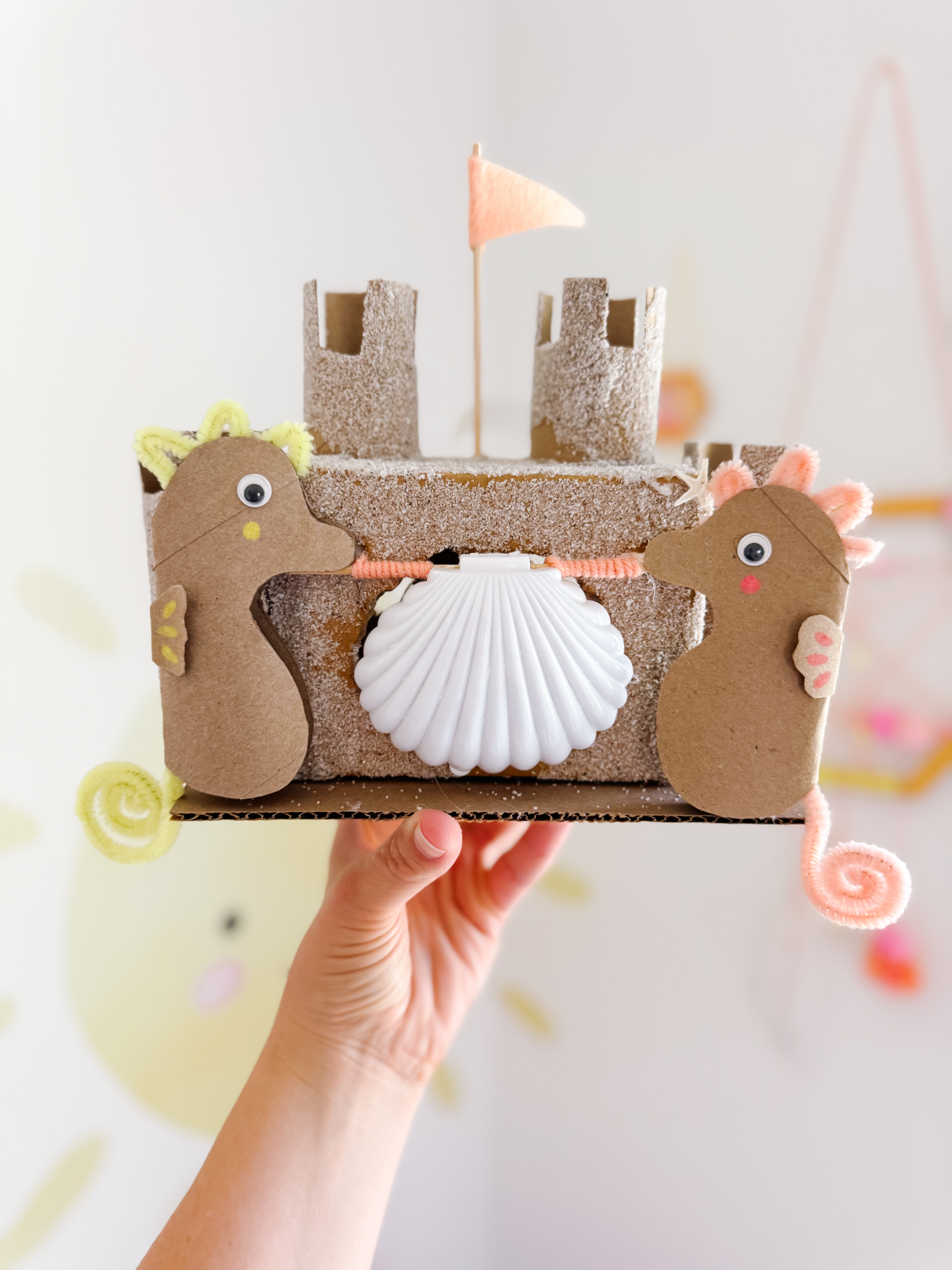 Two cardboard seahorses playing in front of a handmade sandcastle with a shell door