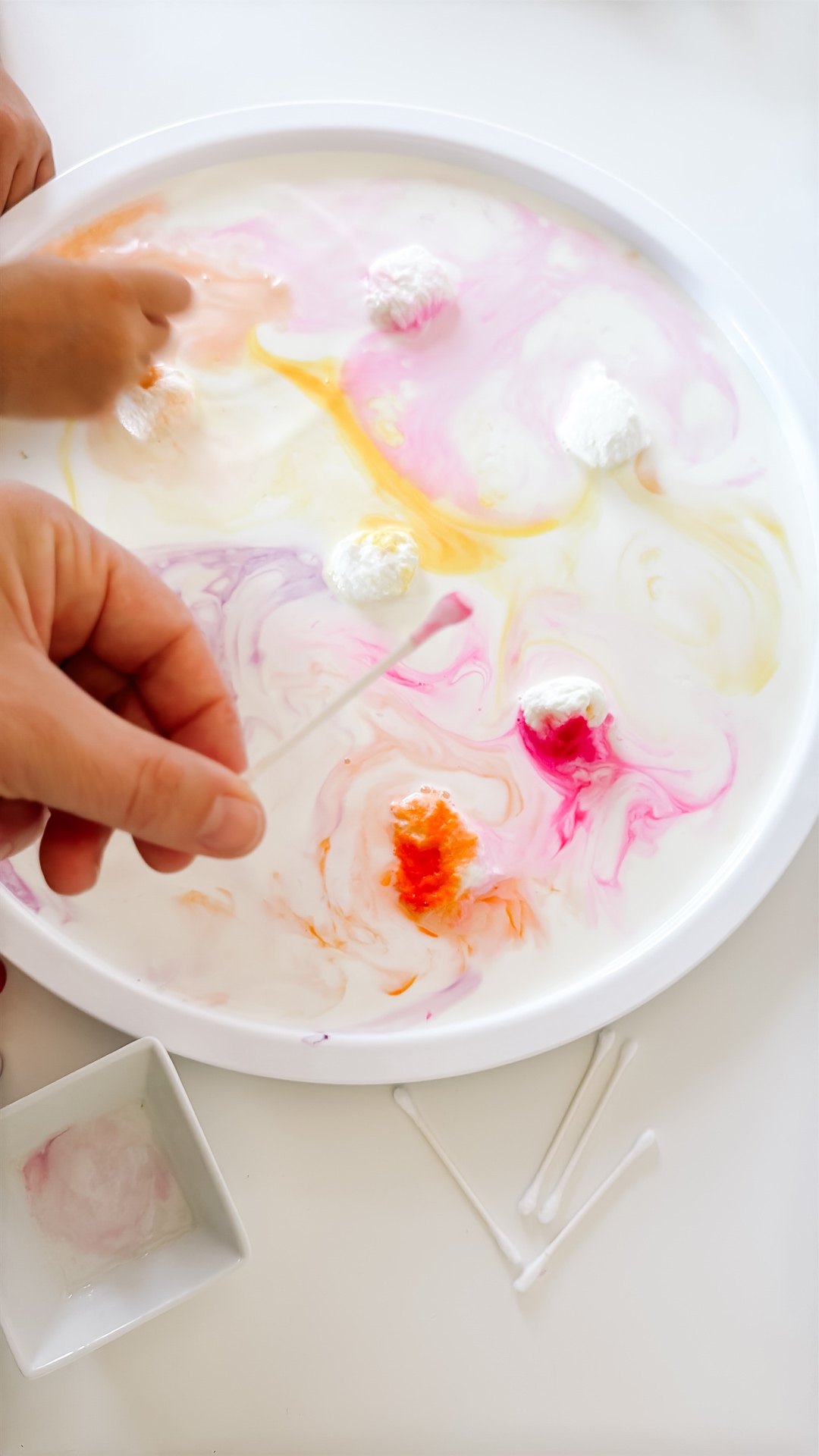 Adult holding a pink-tipped cotton swab over the warm-colored milk experiment