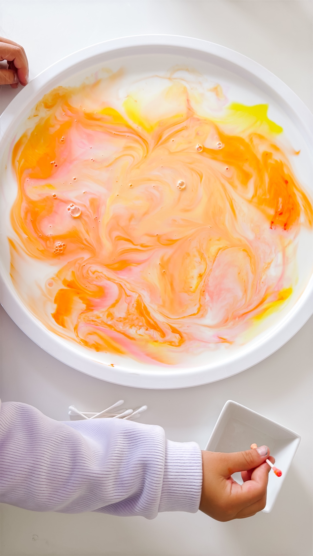 Warm yellow, orange, and pink sunset colors swirling across a plate of milk