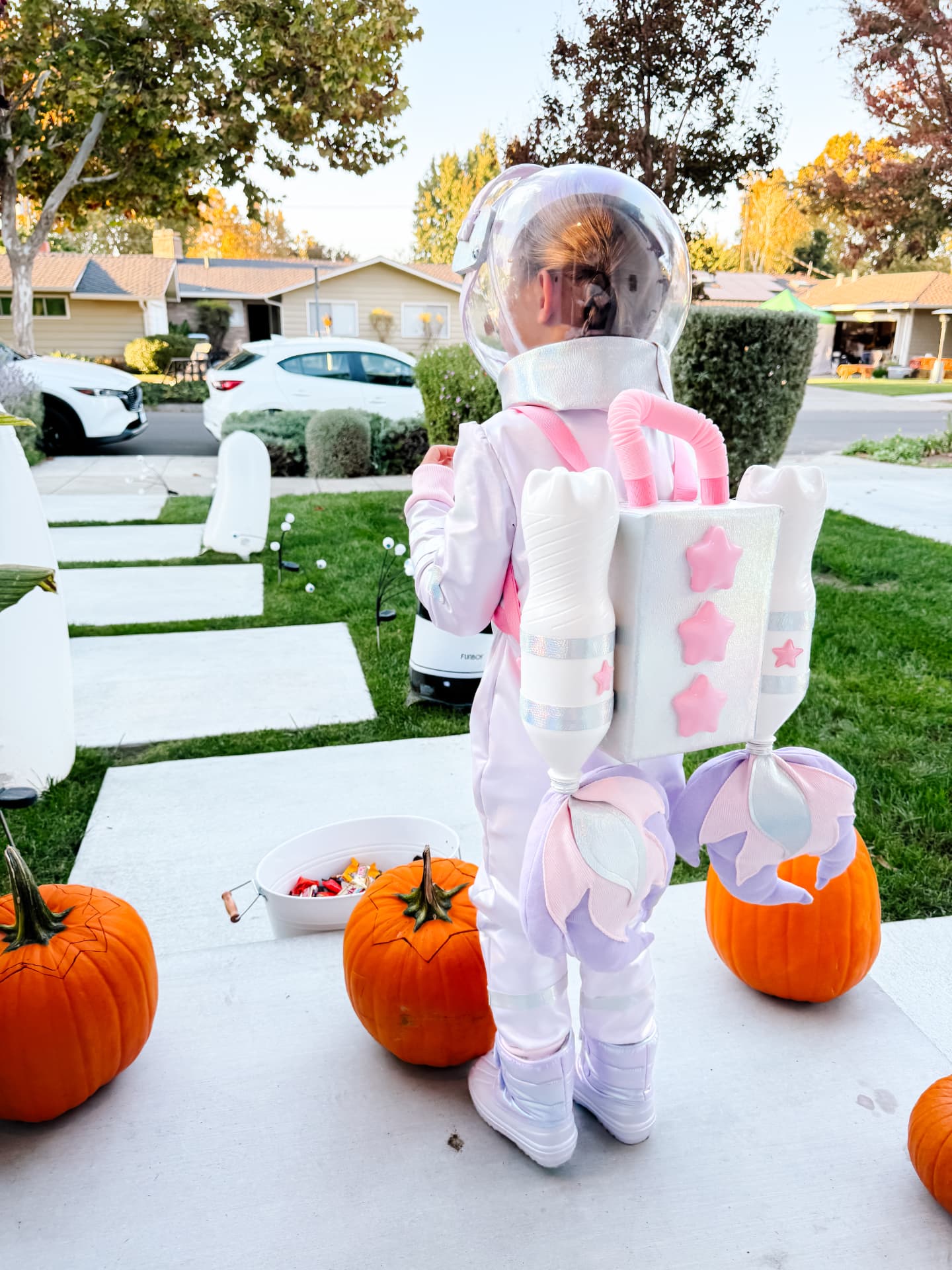 Little astronaut wearing the jetpack outdoors beside pumpkins