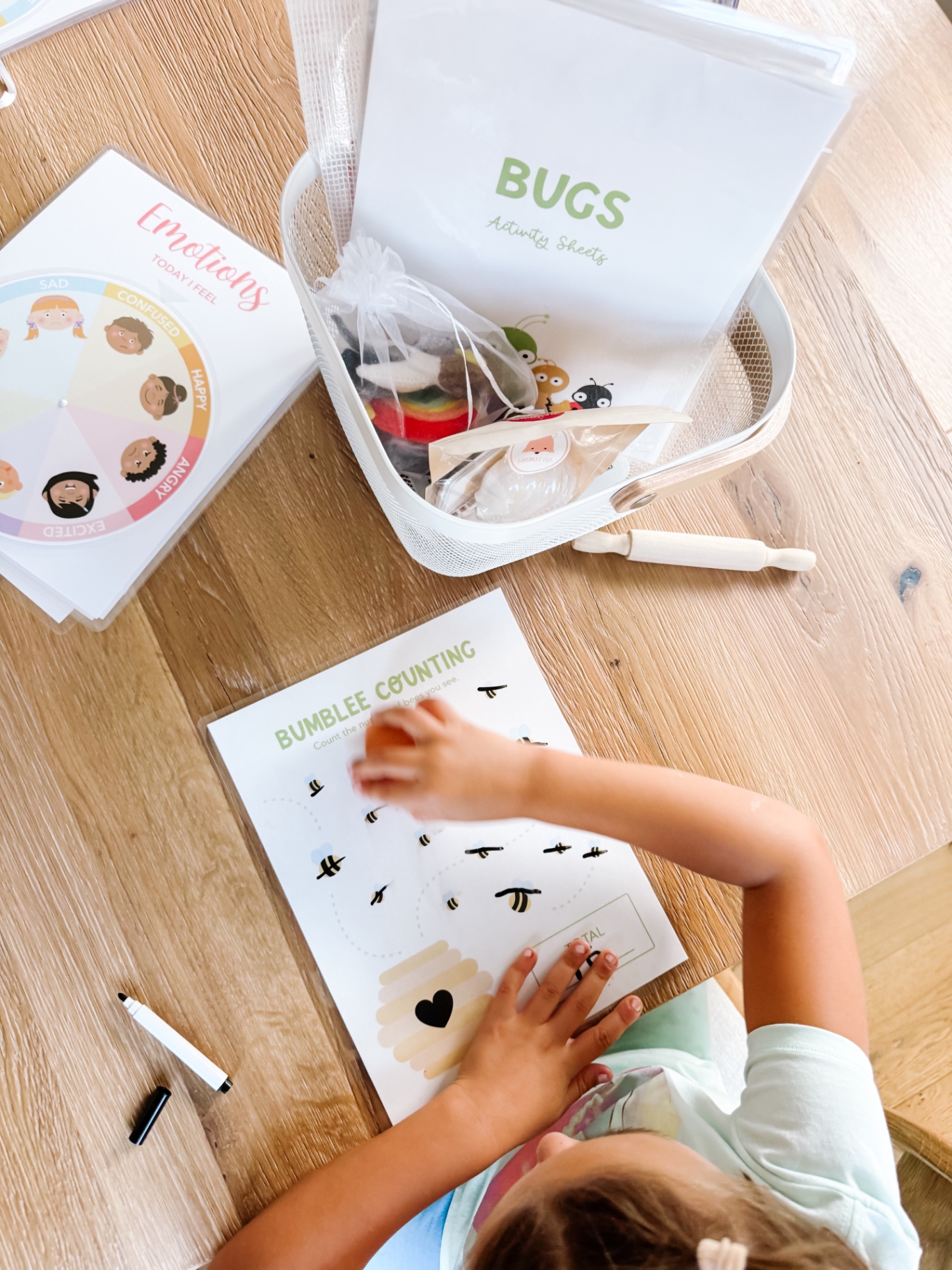 Child counting bumblebees on a bug activity sheet beside a basket of felt bugs